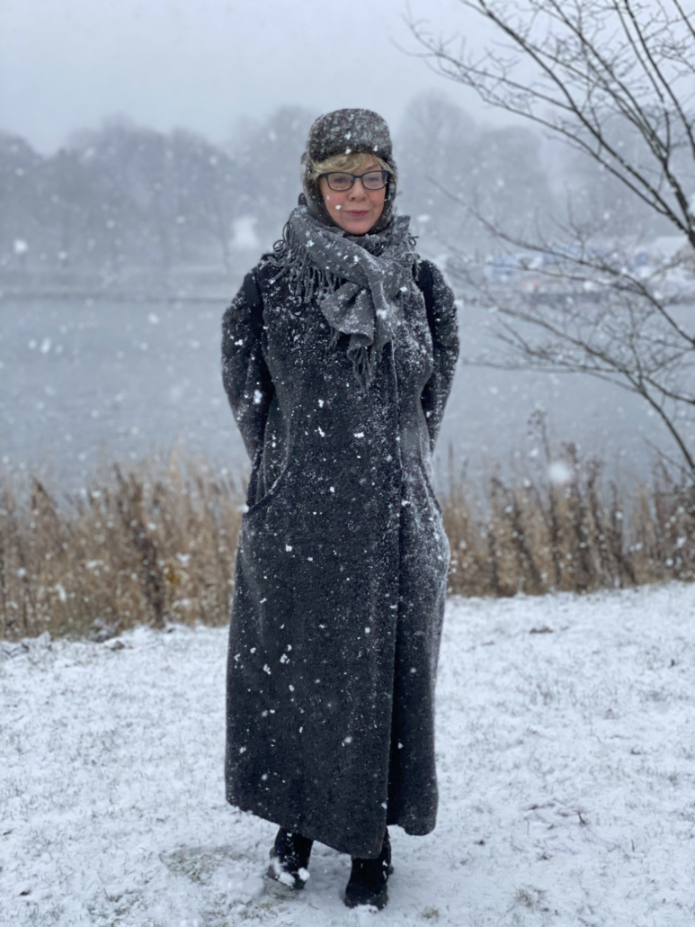 Gunhild Arby i lång vinterkappa och mössa bland en massa snöflingor.