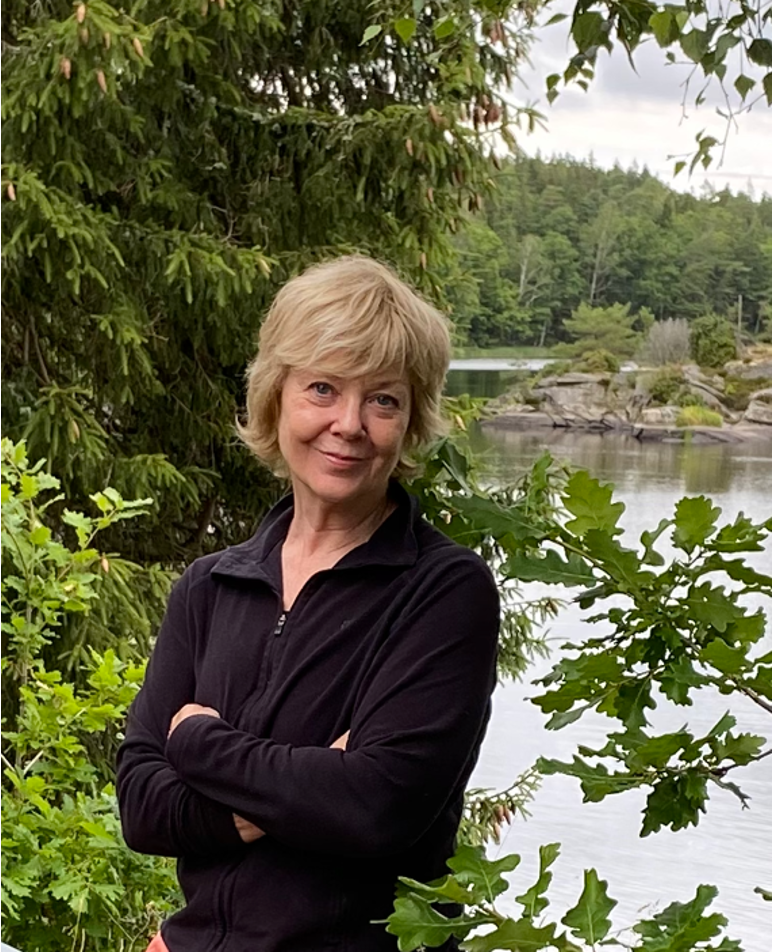 Bild på Gunhild Arby som ler framför grönska och sjö i bakgrunden