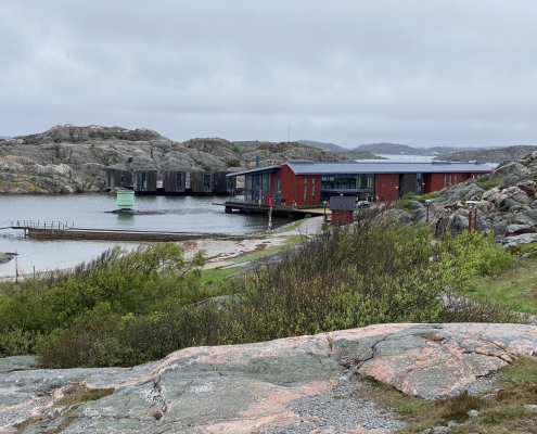 Bild på gul granitklippa i förgrunden och länge ner står det röda akvarellmuseet i Skärhamn vid klippor och vatten